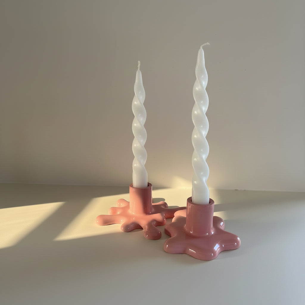 Two white spiral candles on pink candle holders against a neutral background