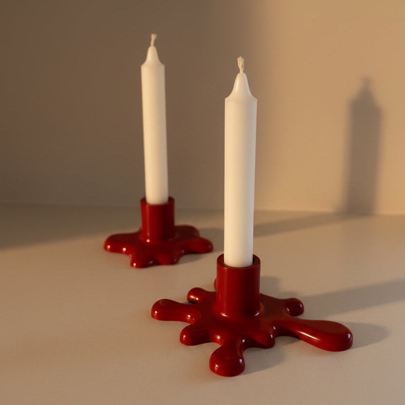 Two white candles in red candle holders on a neutral background