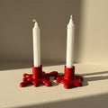 Two white candles in red candle holders on a neutral background