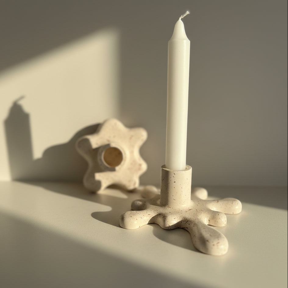 Speckled porcelain candle holder with a white candle on a plain background