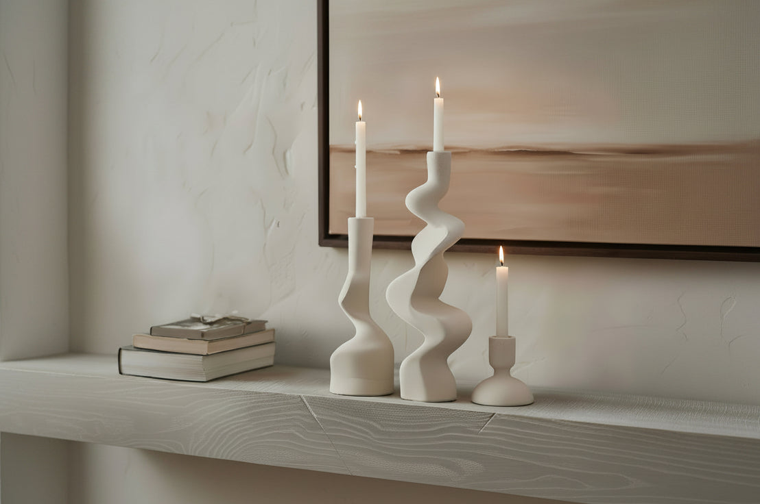 Three white candle holders with candles on a shelf against a neutral wall.