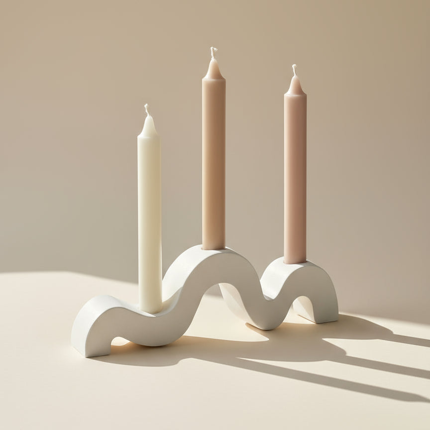 White wavy candle holder with three candles on a reflective surface
