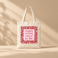 An off-white canvas tote bag with two handles, featuring a square graphic print on the front. The print has a light pink background with the words 'enjoy every curve in life' in dark red text, surrounded by a red wavy pattern.